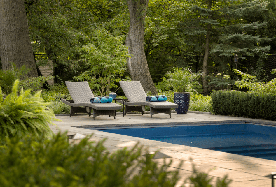 Lounge seating by the pool in a backyard surrounded by mature trees